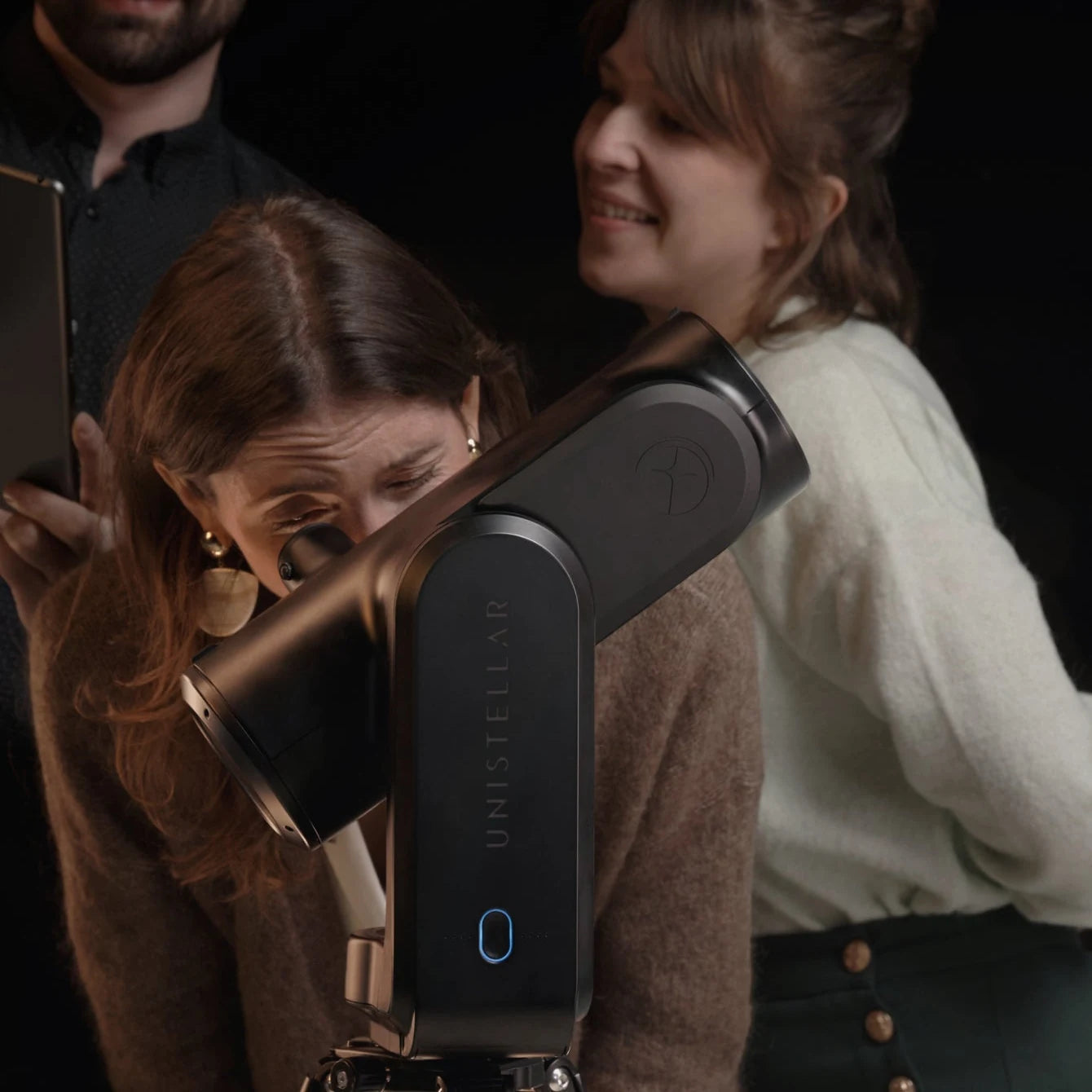 Observer looking through the Nikon eyepiece of the Unistellar Odyssey Pro while friends watch on a tablet